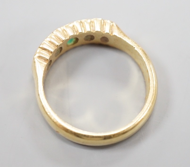 A modern 18ct gold and graduated five stone emerald set half hoop ring, with diamond chip spacers, size Q/R, gross weight 7.5 grams.
